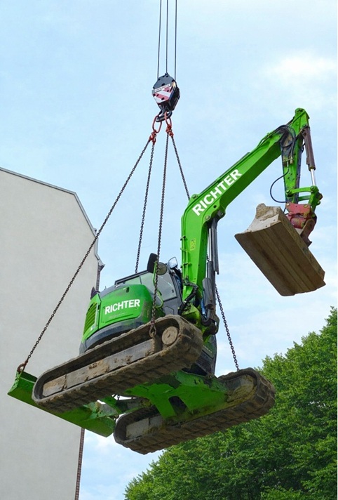 Bagger wird per Kran aus Baugrube gehoben in Hamburg